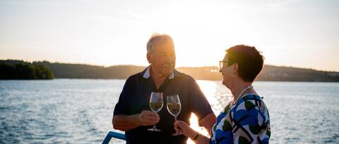 Ein Mann und eine Frau stehen an der Reling und stoßen mit einem Glas an