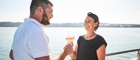 Ein Mann und eine Frau stehen an der Reling und stoßen mit einem Glas an