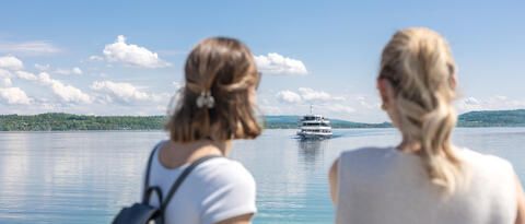 Zwei Frauen stehen am Schiffsanleger und blicken auf das heranfahrende Schiff.