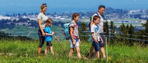 Eine Familie wandert auf dem Witzweg im Appenzellerland. Im Hintergrund sieht man den blauen Bodensee.