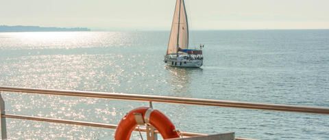 Sicht von einem Schiff der Bodensee Schifffahrt mit einem Rettungsring, auf ein ruhig liegendes Segelboot auf dem Bodensee. 