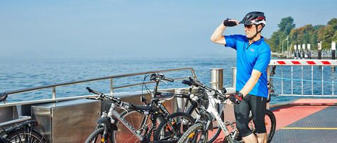 Fahrradfahrer der auf dem Deck der Faehre die Aussicht über den Bodensee genießt.