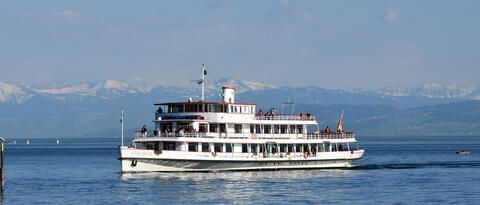 Das Schiff "MS Karlsruhe" fahrend auf dem Bodensee mit den Bergen im Hintergrund.