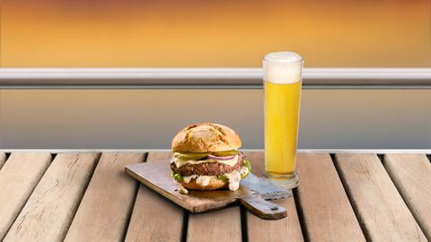 Büffel-Burger mit einem voll gefüllten Bier und einem Sonnenuntergang im Hintergrund.