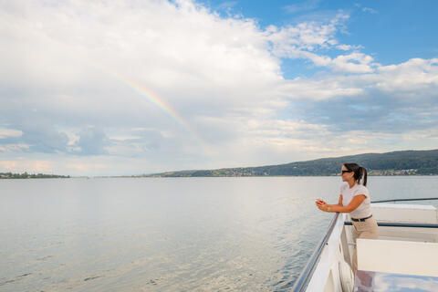 Eine Frau lehnt an der Reling. Im Hintergrund ist ein Regenbogen zu sehen