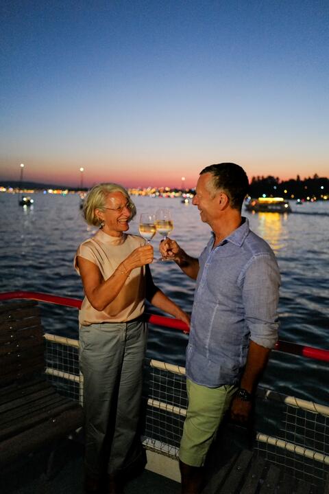Ein Pärchen stößt in der Abenddämmerung an Bord mit einem Glas Wein an