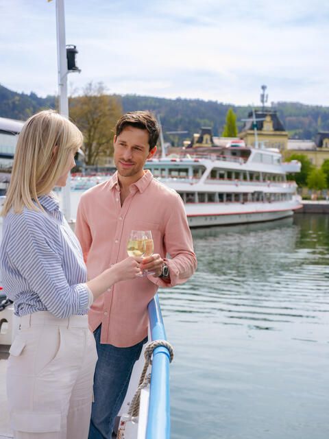 Ein Mann und eine Frau stehen an der Reling und stoßen mit einem Glas an