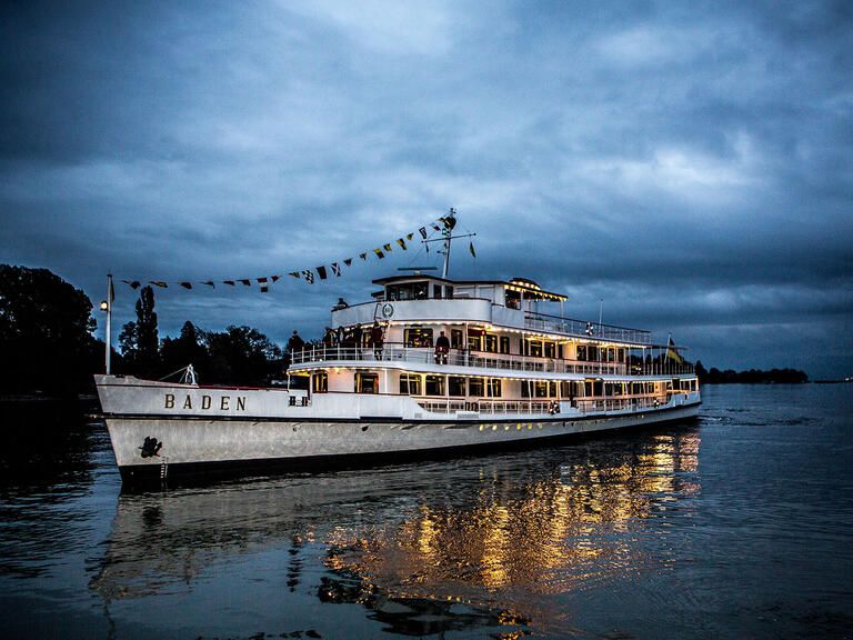 Die beleuchtete "MS Baden" bei Dämmerung auf dem Bodensee.