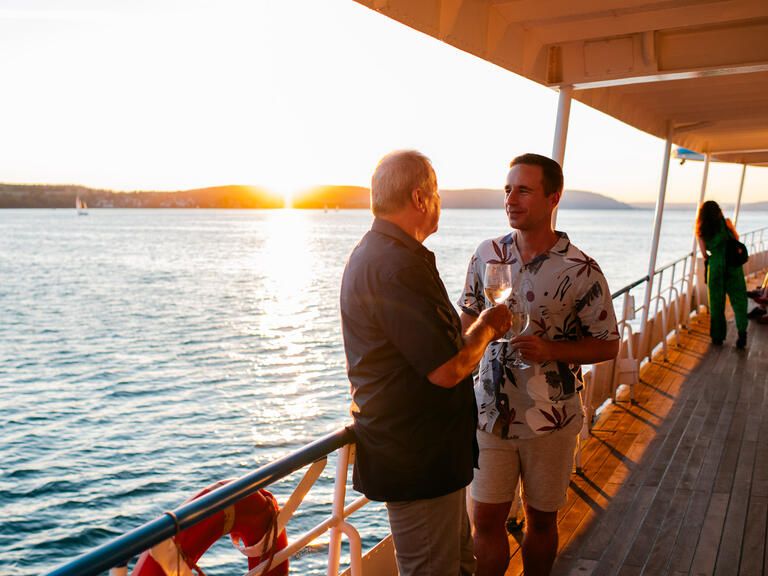 Zwei Männer stehen an der Reling auf einem Schiff der BSB, sie unterhalten sich, im Hintergrund geht hinter dem See die Sonne unter.