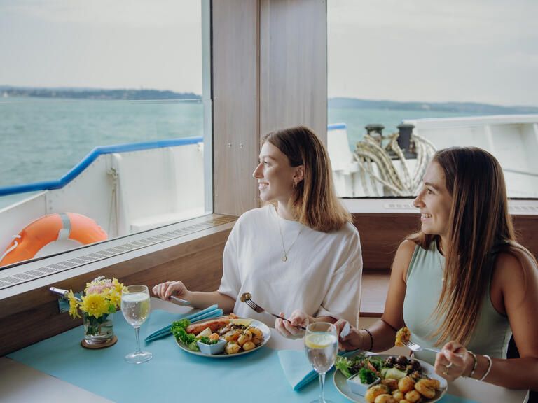 Zwei Frauen bei einer Fahrt mit dem Schiff, die einen Lachsteller essen