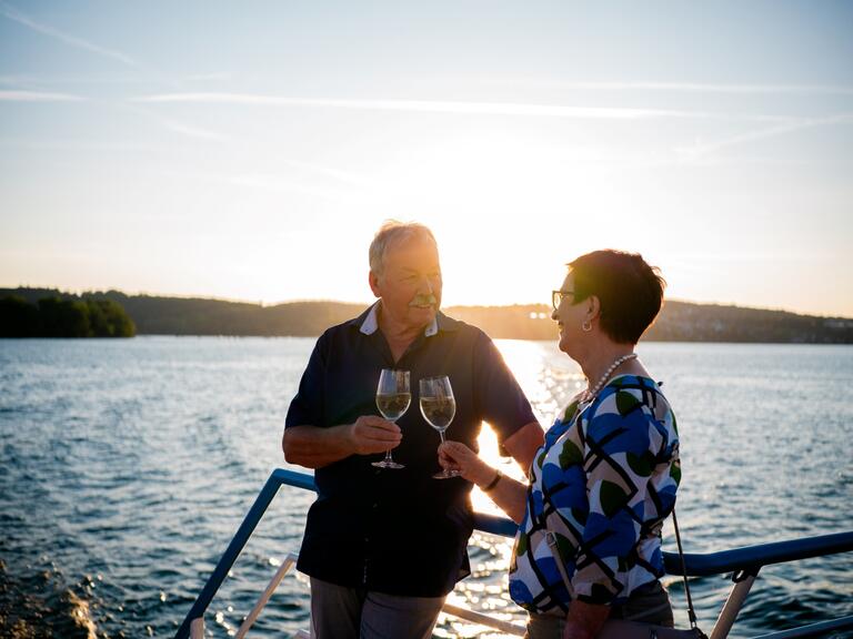 Ein Mann und eine Frau stehen an der Reling und stoßen mit einem Glas an