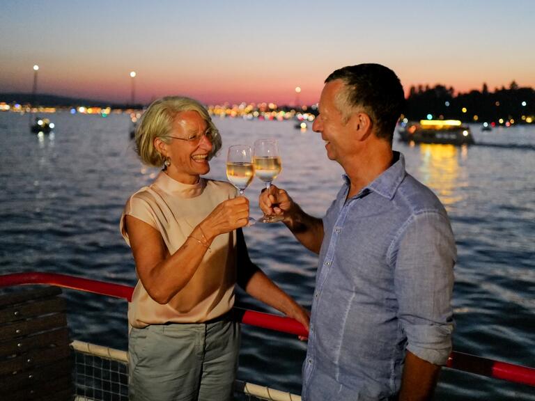 Ein Pärchen stößt in der Abenddämmerung an Bord mit einem Glas Wein an