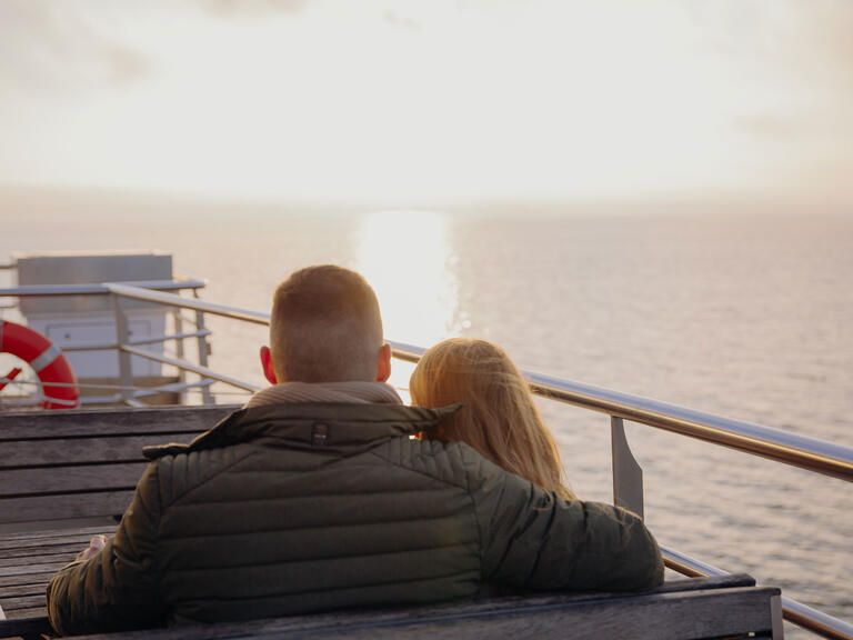 Ein Pärchen genießt den Ausblick auf den glitzernden Bodensee im Abendlicht.