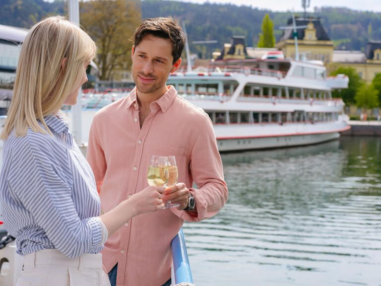 Ein Mann und eine Frau stehen an der Reling und stoßen mit einem Glas an