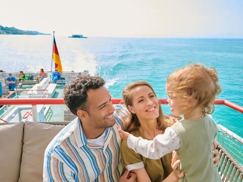 Familie mit Kleinkind auf dem Schiff, alle lachen, im Hintergrund der Bodensee
