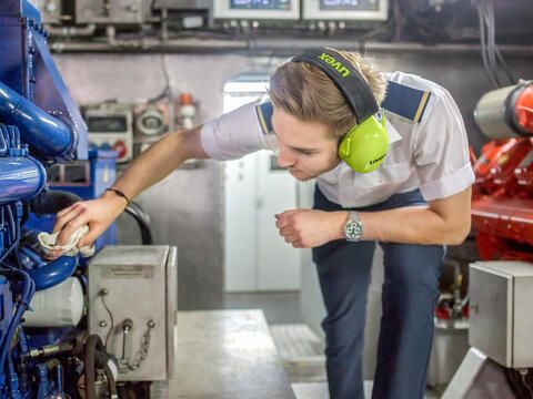 Ein Mitarbeiter der BSB in Uniform putzt bzw. arbeitet an einer Maschine im Maschinenraum.