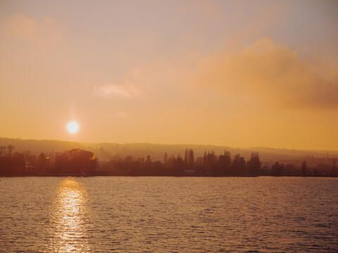 Der Sonnenuntergang taucht den See und die Uferlandschaft in ein goldenes Licht