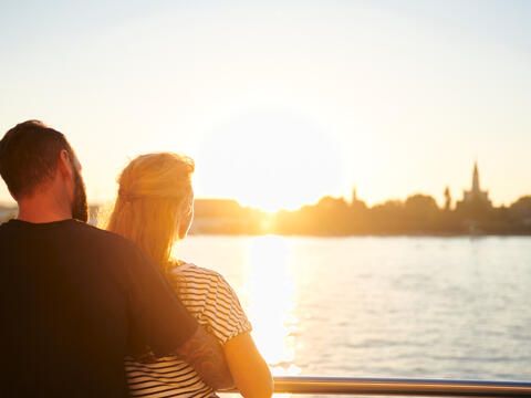 Paar schaut auf einer Bodensee-Schifffahrt in die untergehende Sonne