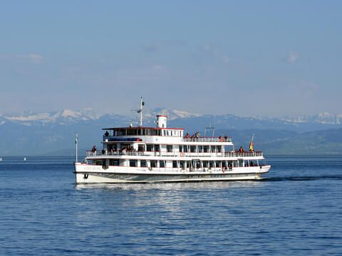 Das Schiff "MS Karlsruhe" fahrend auf dem Bodensee mit den Bergen im Hintergrund.